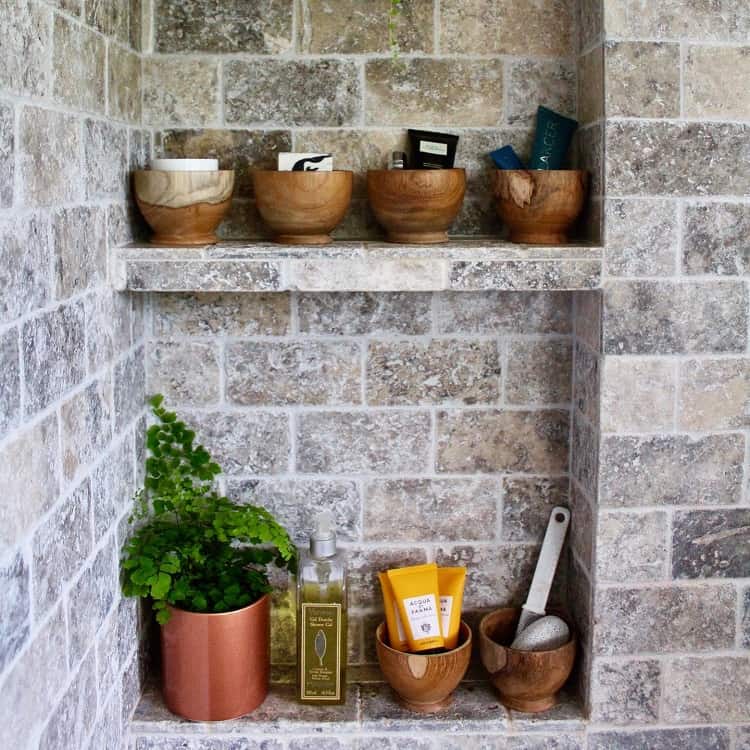 Stone bathroom shelf with wooden bowls, toiletries, and a potted plant.