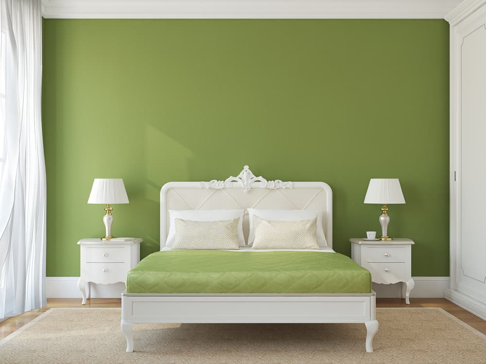 A bedroom with a green accent wall, white bed and furniture, and two lamps on nightstands