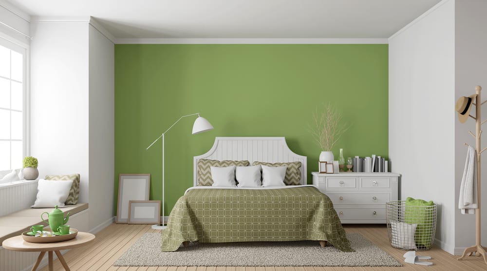 A cozy bedroom with a green accent wall, white bed, matching bedding, and a window seat. Decor is minimal and modern