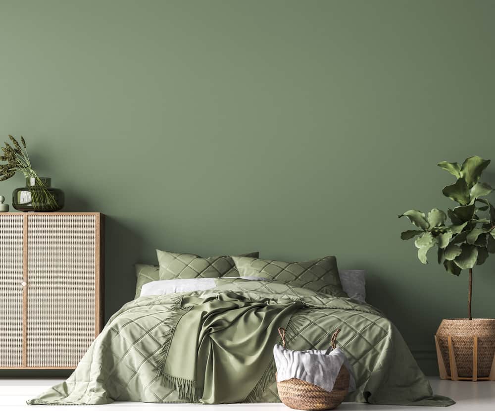 A green bedroom with a neatly made bed, plants, and a wicker basket on a wooden floor