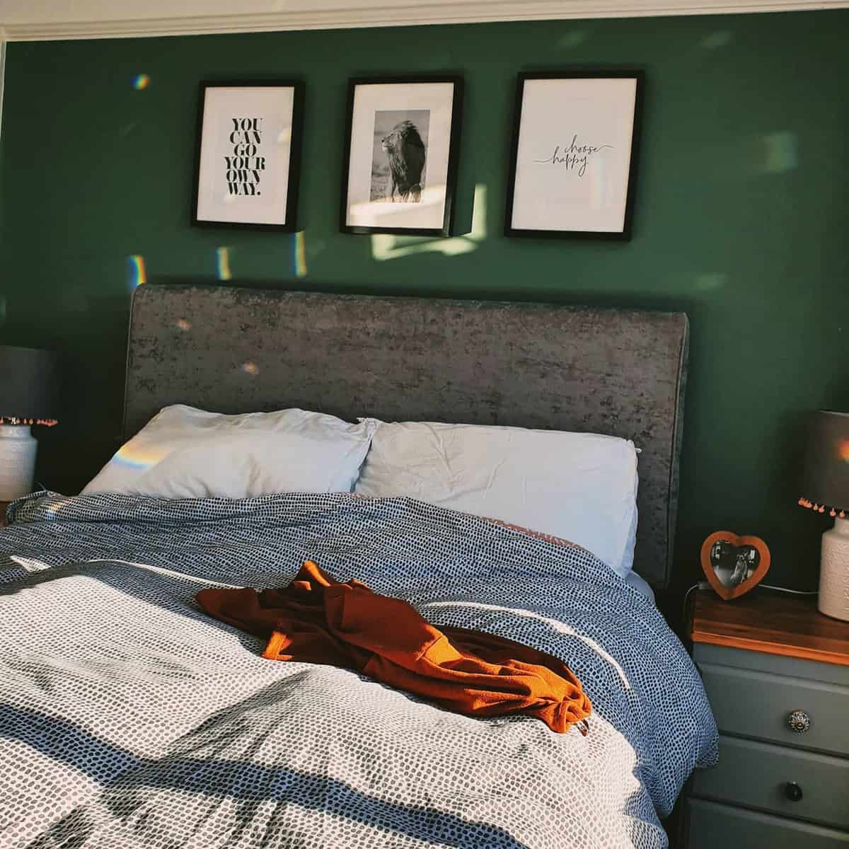 Cozy bedroom with gray bed, green wall, framed art, and sunlight casting shadows on the bedding