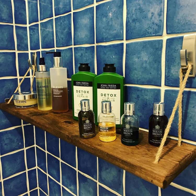 Wooden bathroom shelf with toiletries and blue tiled wall backdrop.