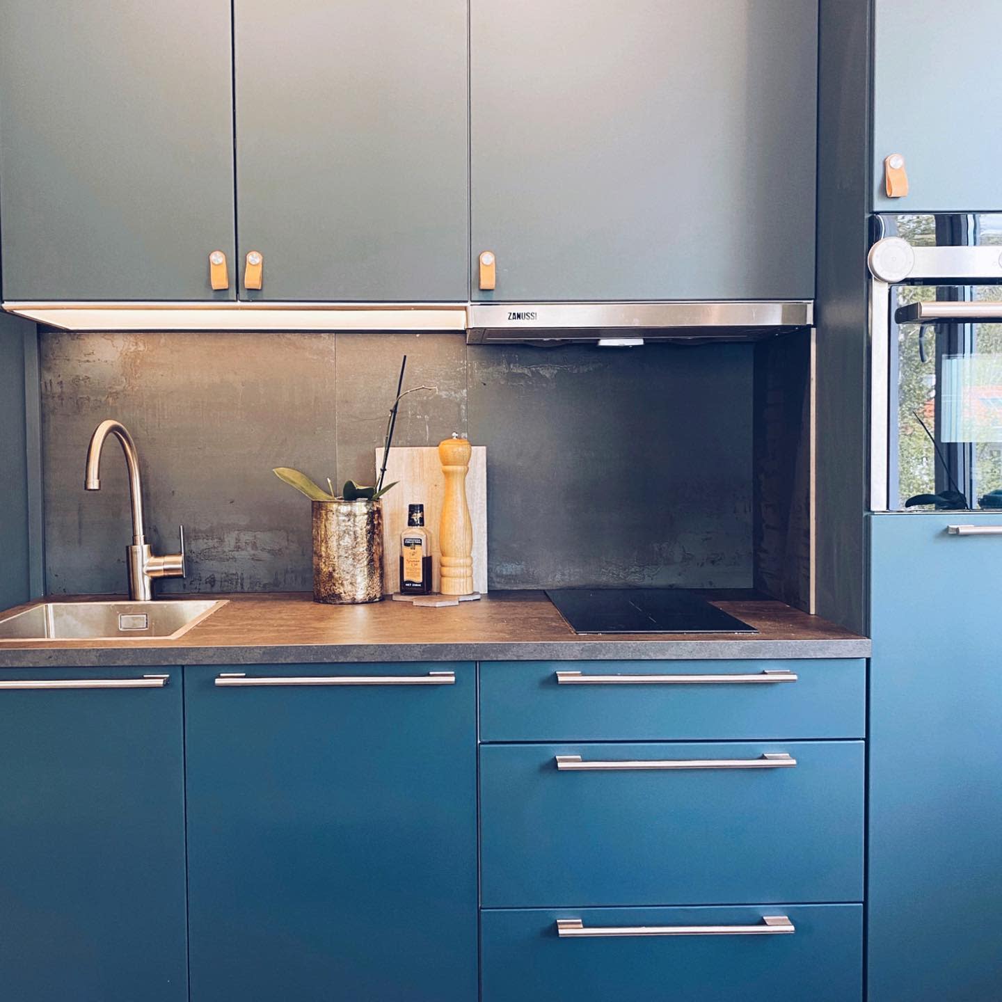 Modern blue kitchen cabinets with built-in oven, stovetop, and stainless steel sink.