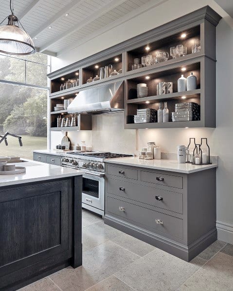 Stylish kitchen with concrete flooring, gray cabinetry, open shelves with glassware, and modern stainless steel appliances