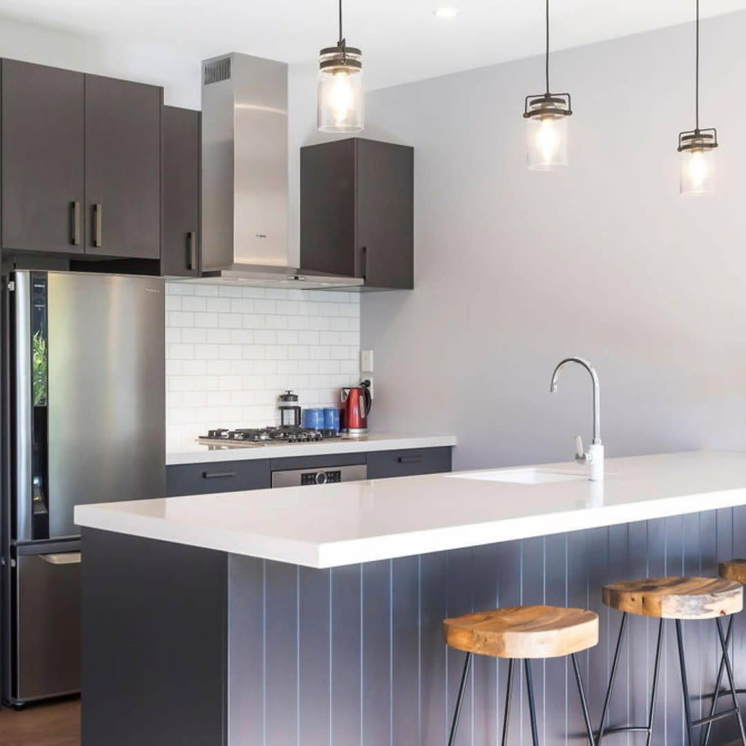 Stylish modern kitchen with black cabinets, white island, bar stools, and pendant lighting.