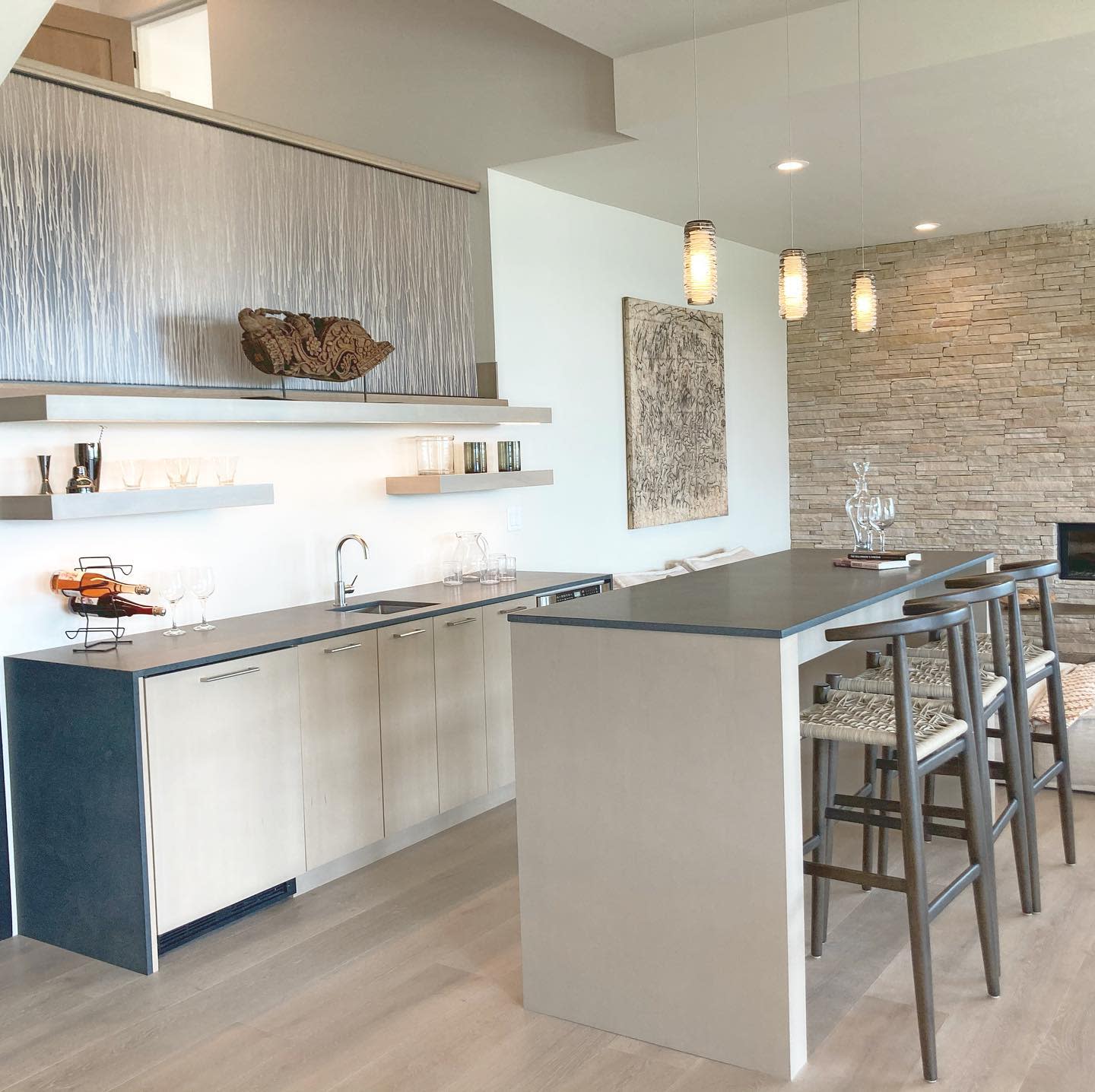 Sleek modern kitchen with island seating, open shelves, and stone accent wall.