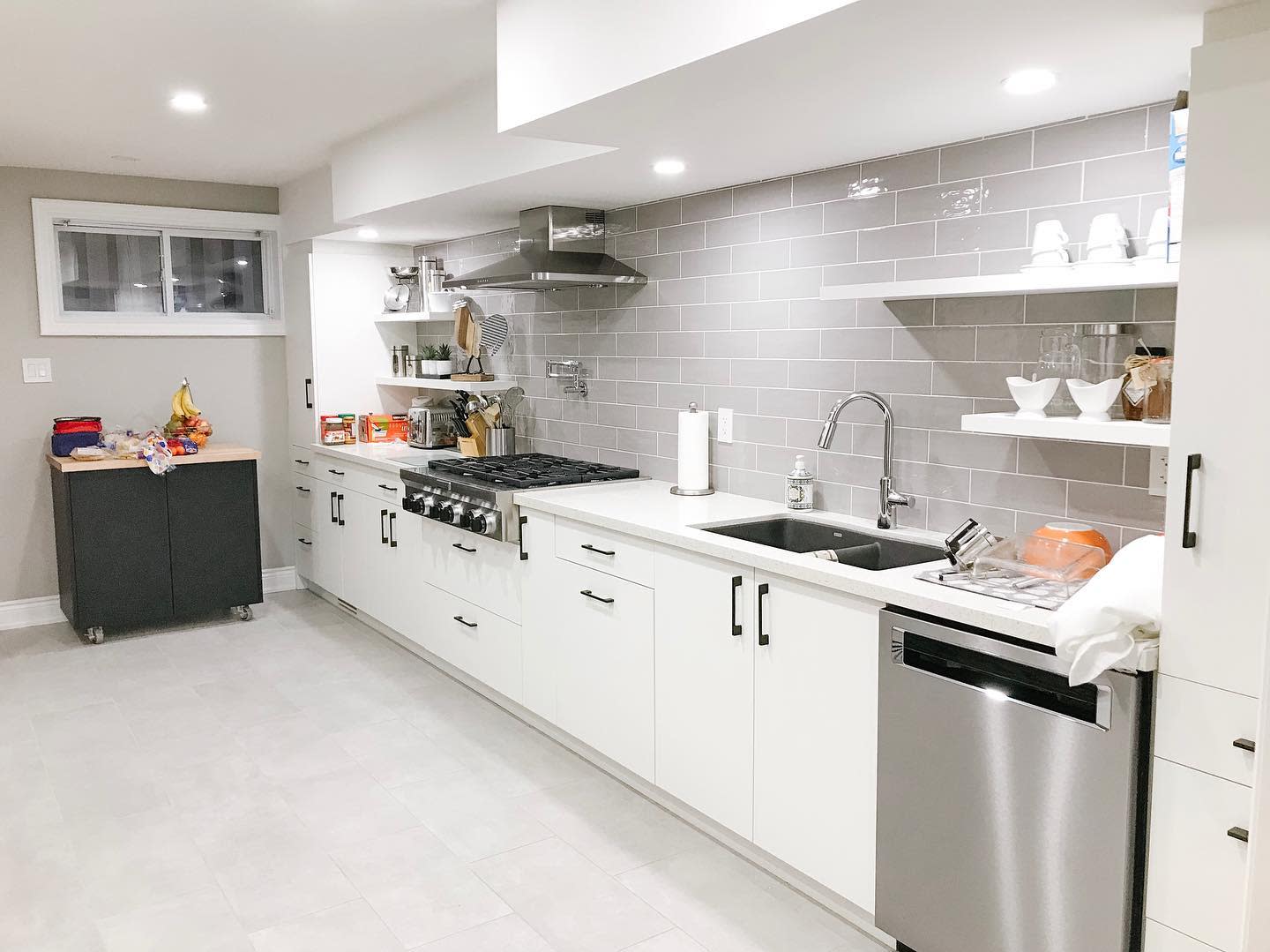 Large white basement kitchen with gray subway tile backsplash and stainless steel appliances.