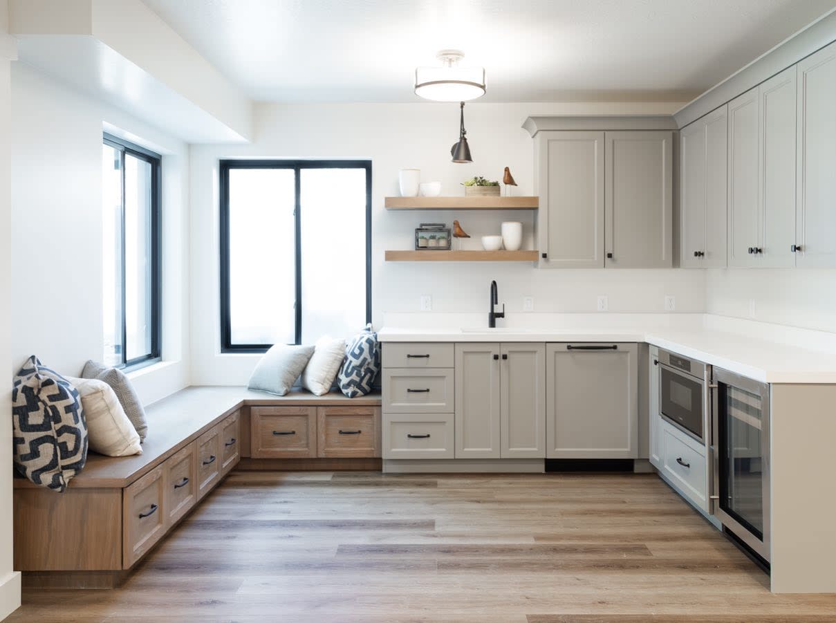 White cupboards with grey wood flooring, built-in seating, and open shelving in kitchen.