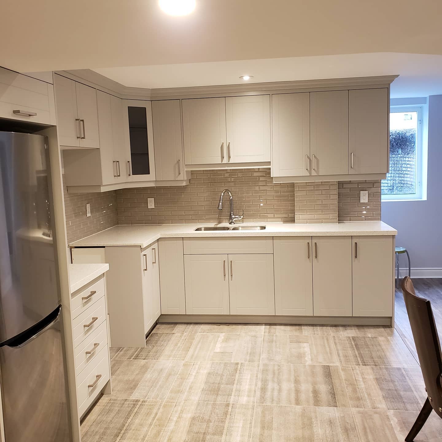 Modern basement kitchen with light grey cabinets, tile backsplash, and stainless steel appliances.