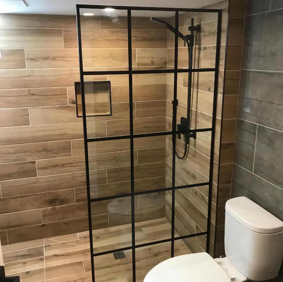 Contemporary shower with black-framed glass door, wood-look tile walls, and modern fixtures.