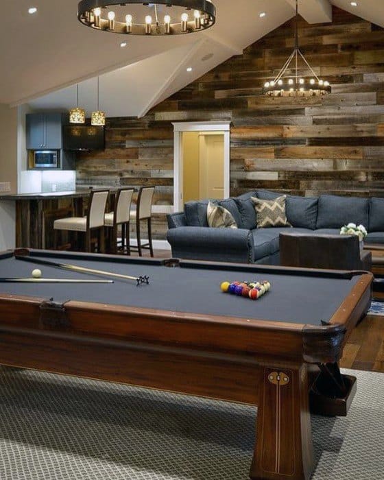 Rustic mancave with wood accent wall, pool table, modern bar, sectional sofa, and vaulted ceiling.