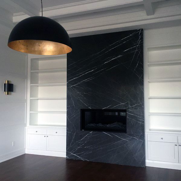 Contemporary black marble fireplace with white built-in shelving on both sides.