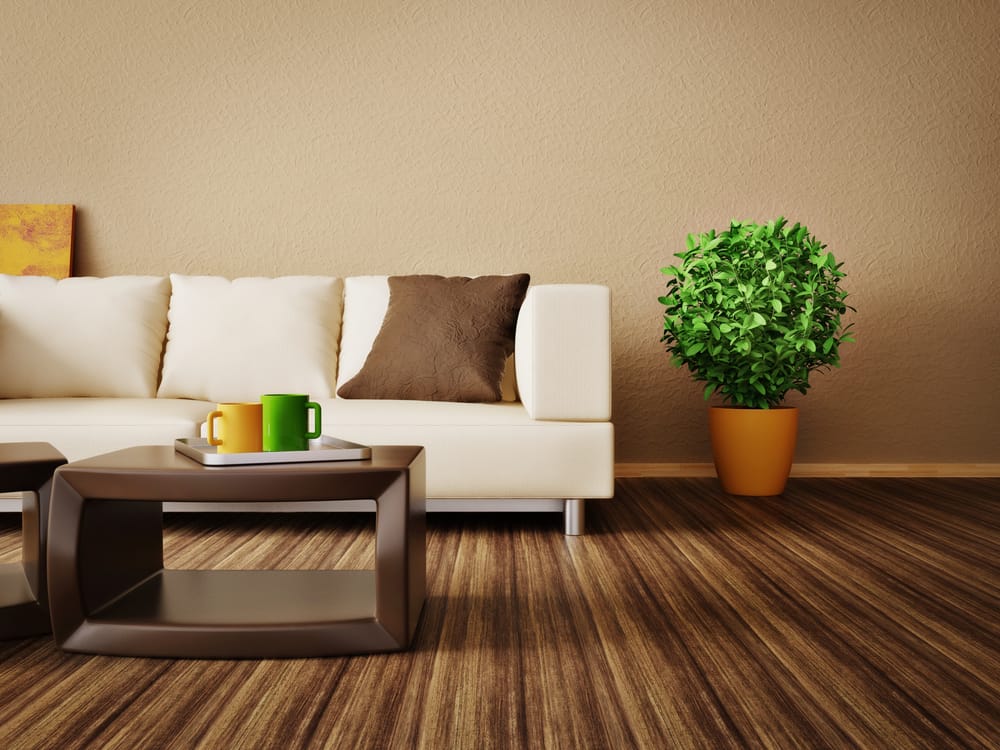 Modern living room with a beige sofa, brown and green cushions, wooden tables, and a potted plant on striped flooring