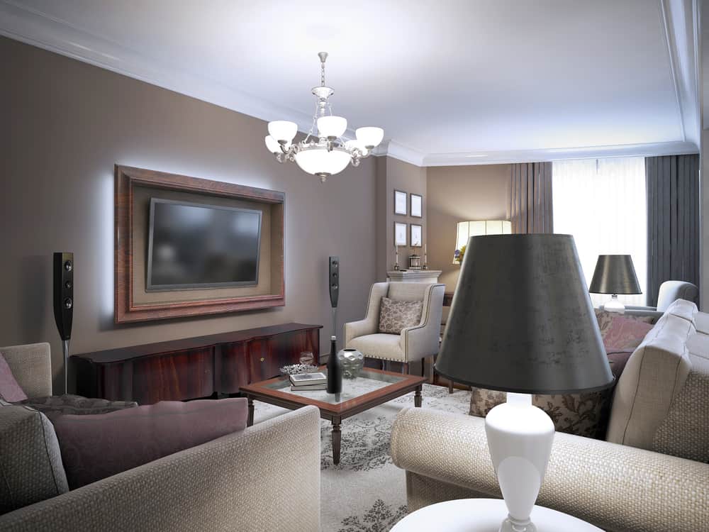 Elegant living room with brown sofas, a coffee table, large TV, and chandelier, lit by natural and lamp light