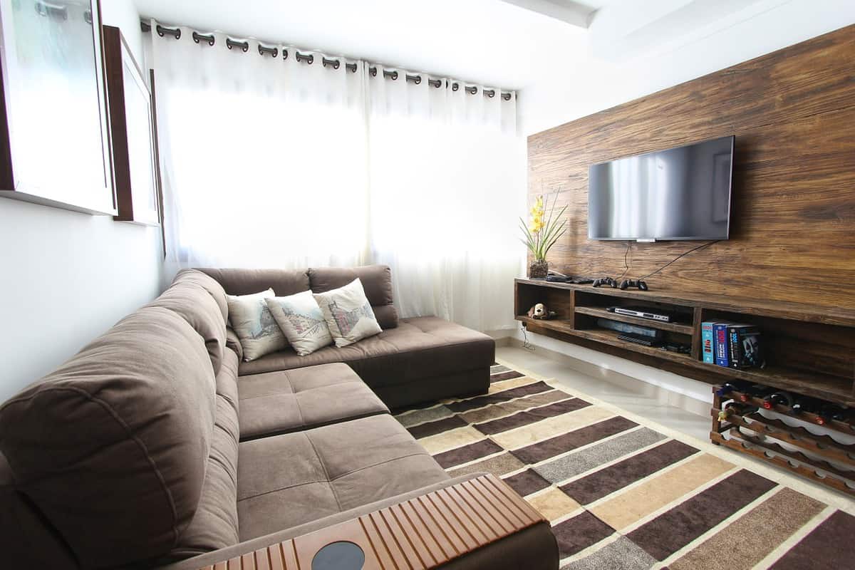 Modern living room with a plush brown sectional, wall-mounted TV, and striped rug on tile floor