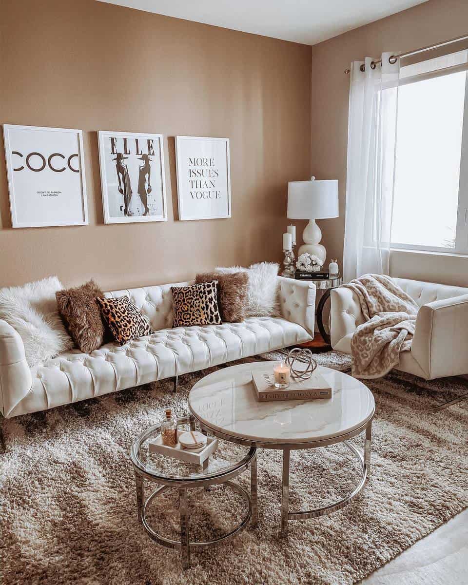 Stylish living room with white sofas, furry pillows, wall art, round tables, and a large window with sheer brown curtains