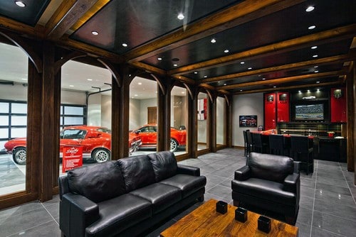 Luxury garage bar with leather seating, wooden beams, red cars on display, and sleek decor.