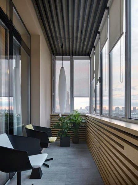 Modern sunroom with black chairs, wood paneling, and large windows at sunset.