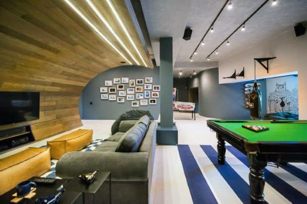 Modern mancave with curved wood accent wall, cozy seating, pool table, and striped flooring.