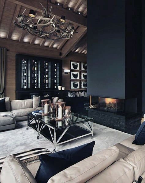 Contemporary living room with a large central fireplace, leather sofas, and antler chandelier.