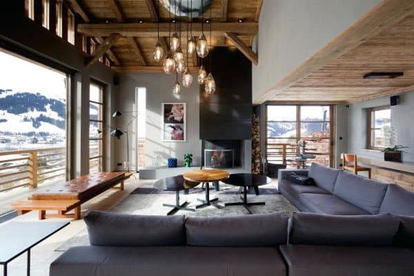 Modern living room with large windows, gray sofas, wood ceiling, fireplace, and a view of snowy mountains