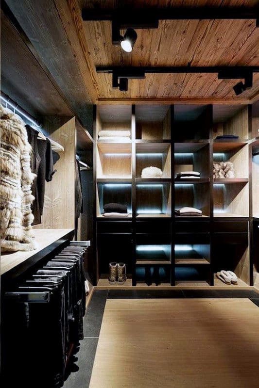 Spacious wooden walk-in closet with shelves, racks, and folded clothes, softly lit from above