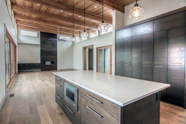 Spacious kitchen with wood-paneled ceiling, white island, dark cabinets, and pendant lighting.