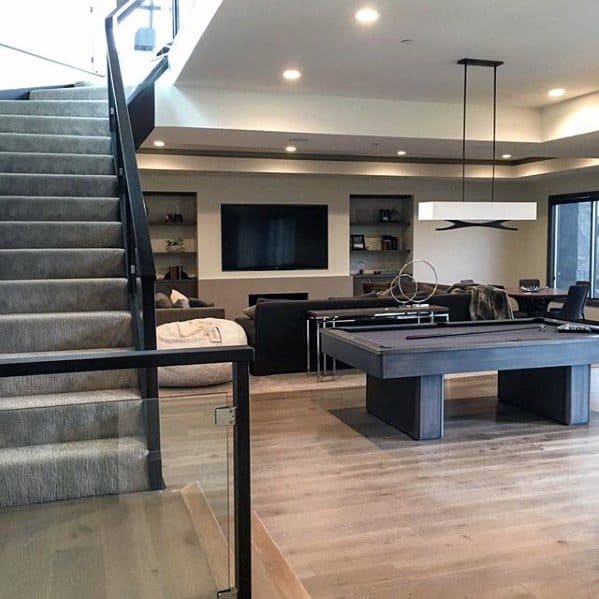 Modern mancave with sleek pool table, large TV, built-in shelves, and open-concept design.