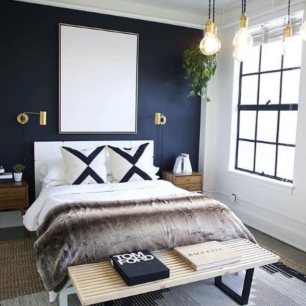 Modern men's bedroom with black accent wall, fur blanket, gold sconces, and hanging lights.