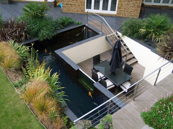 Elevated tiled pond with surrounding plants, featuring a sunken patio dining area with modern furniture.