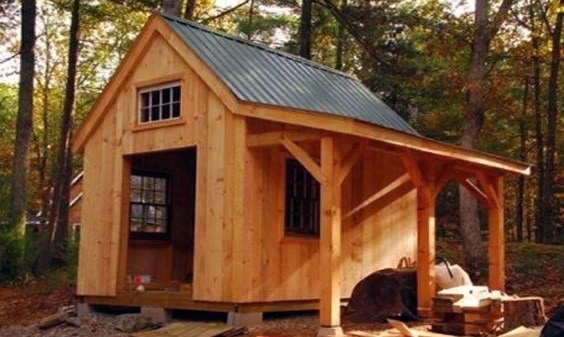 Wooden shed with metal roof, front porch, and rustic charm in a forested backyard.