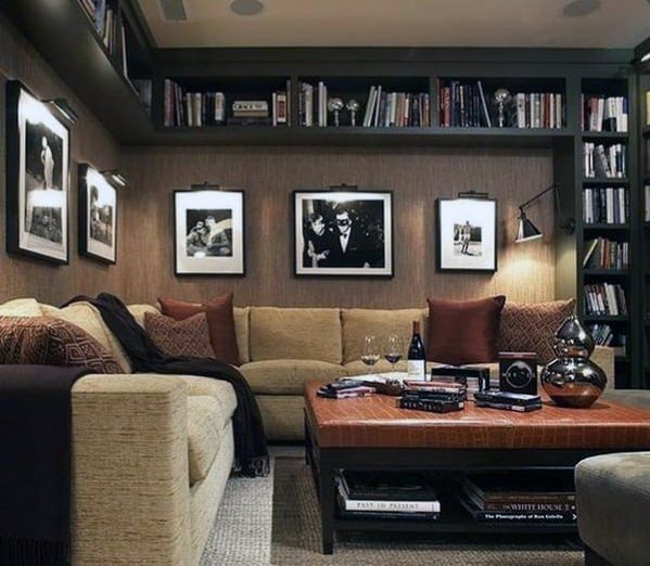 Cozy study with beige sectional sofa, built-in bookshelves, black-and-white photos, and warm lighting.