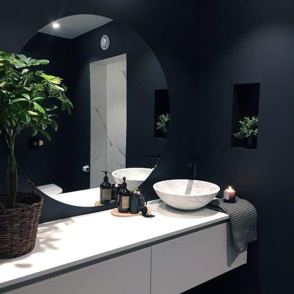 Modern bathroom with black walls, large round mirror, vessel sink, and potted plant on vanity.