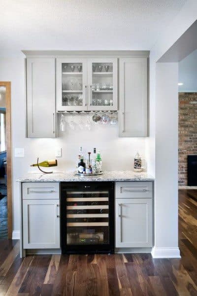 Small home bar with gray cabinets, wine fridge, glass storage, and granite countertop.