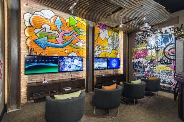 A modern room with graffiti walls, multiple screens, and circular seating, designed for gaming or entertainment