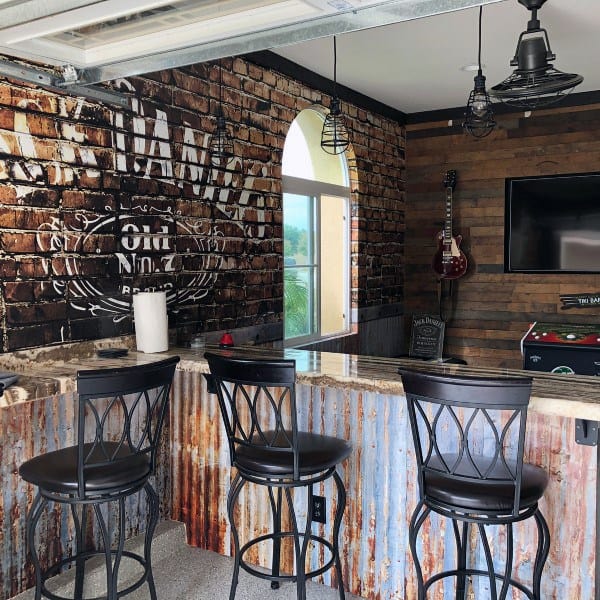 Garage bar with brick walls, corrugated metal bar, black stools, and Jack Daniel's decor.