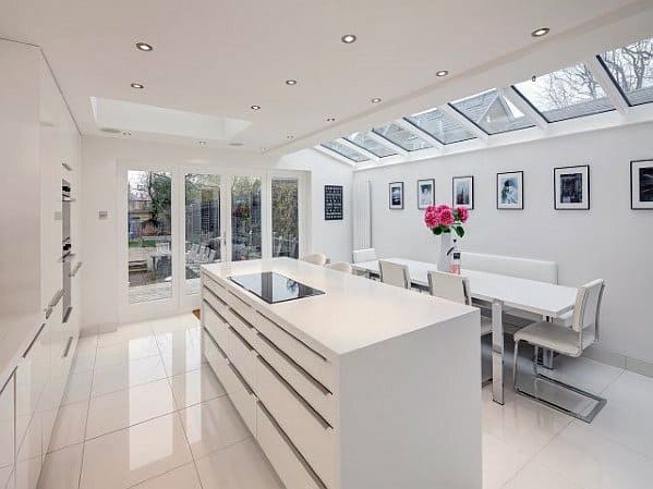 Modern kitchen with white tile flooring, sleek white cabinetry, large island, and abundant natural light from skylights