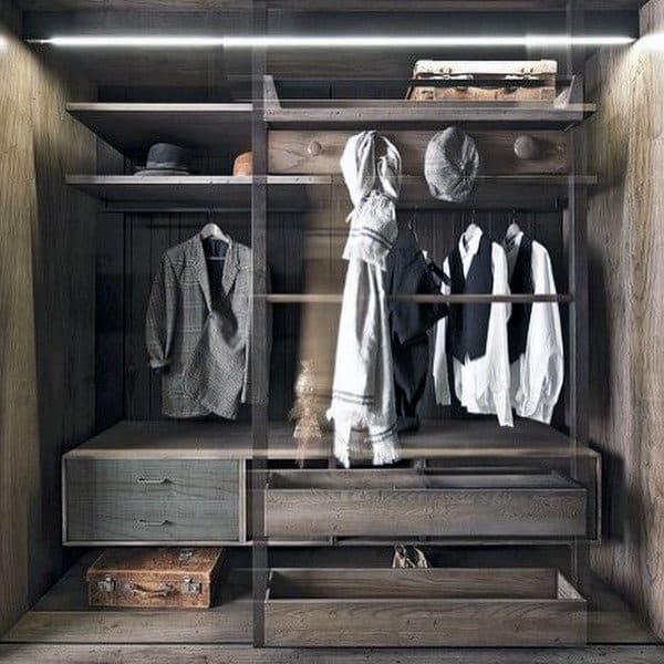 Open wardrobe with hanging clothes, hats, and a suitcase at the bottom. Dark wood and modern design