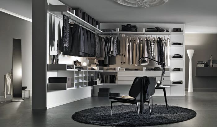 Modern walk-in closet with hanging clothes, shelves, black chair, and circular rug