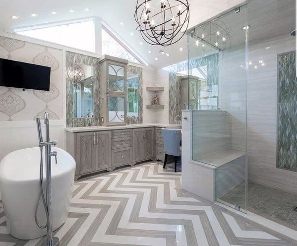 Large bathroom with freestanding tub, seated glass shower, gray vanity, and herringbone tile floor.