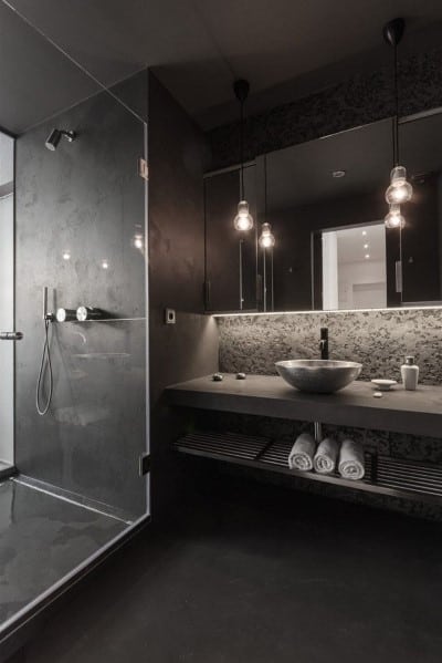 Modern black bathroom with glass shower, stone sink, and industrial pendant lighting.