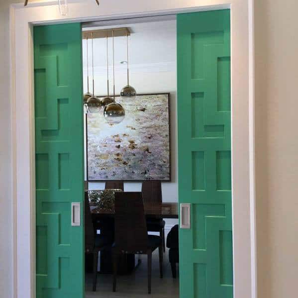 Vibrant green pocket doors with geometric patterns open to a modern dining room featuring pendant lights and wall art