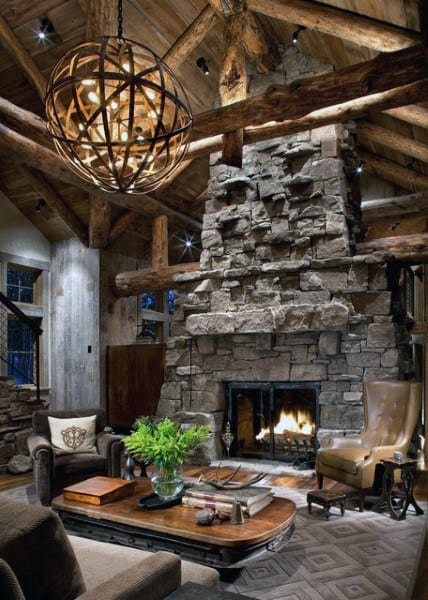 A cozy rustic living room with a stone and wood-burning fireplace, wooden beams, a unique chandelier, and comfortable seating for a warm, inviting atmosphere