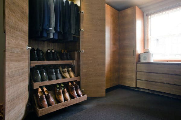 Wooden closet with suits and pull-out shoe shelves, next to window with drawer unit in lit room