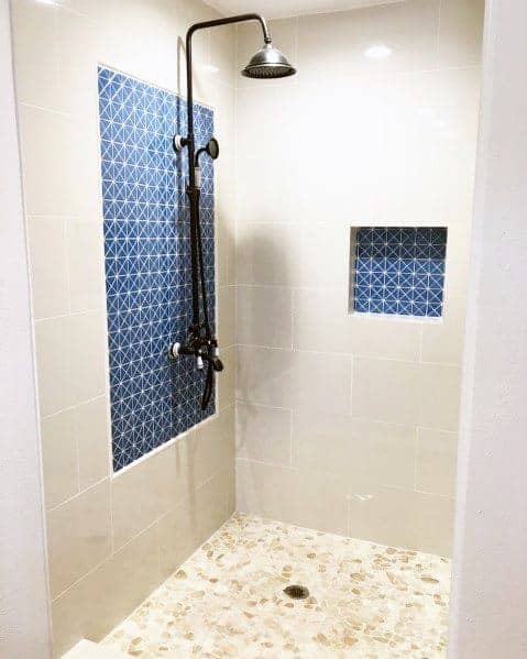 Walk-in shower with blue geometric tile accents, black fixtures, and pebble stone flooring.