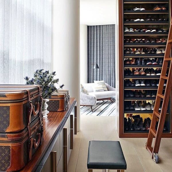 Luxurious walk-in closet with stacked designer suitcases, a tall shoe rack, and a glimpse of a stylish sitting area