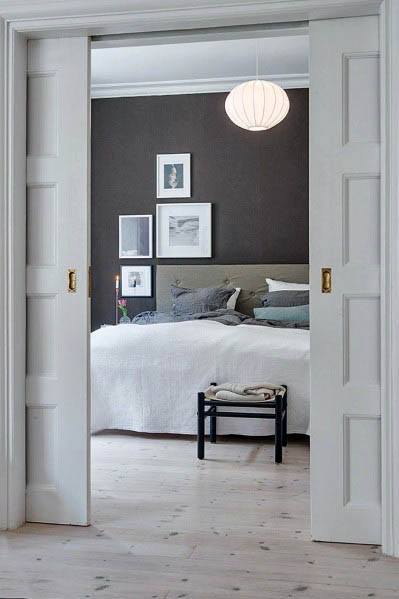 Classic white pocket doors with brass handles open to a cozy bedroom featuring a dark accent wall, gallery frames, and soft bedding