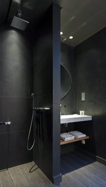 Modern bathroom with sleek black tiled shower, wall-mounted sink, round mirror, and folded towels on a shelf