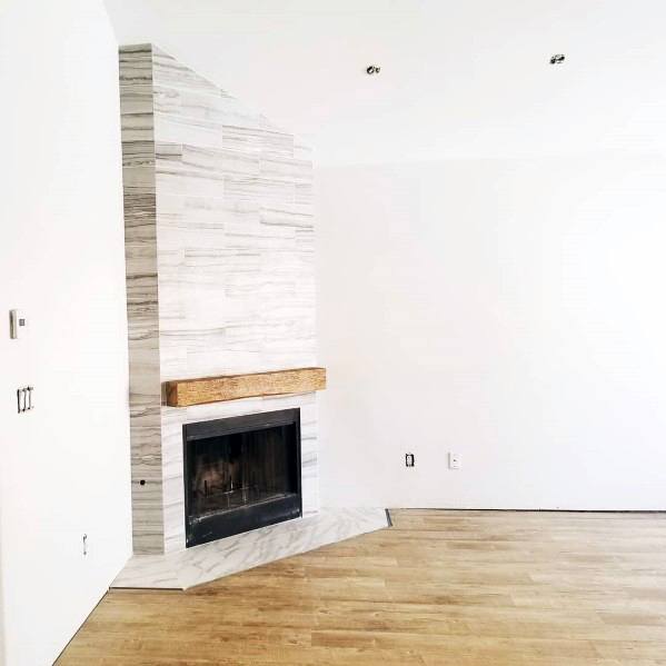 Corner fireplace with white stacked tiles, wooden mantel, and marble hearth.