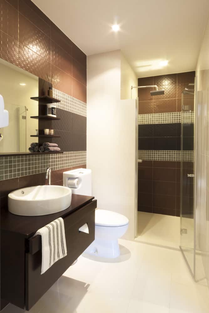 Modern bathroom with brown tiles, glass shower, vessel sink, and floating vanity.